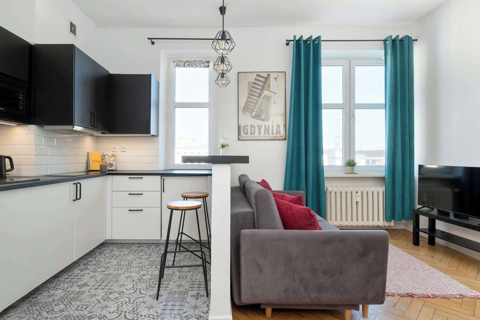 This wide shot captures the open-concept layout connecting the kitchenette and living area. A breakfast bar serves as a divider between the patterned kitchen floor and the wooden floor of the lounge.