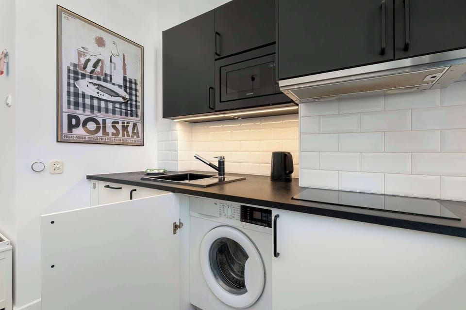 This kitchenette view shows the lower cabinetry with an integrated washing machine hidden behind a white door. The setup demonstrates a smart use of space for essential home appliances.