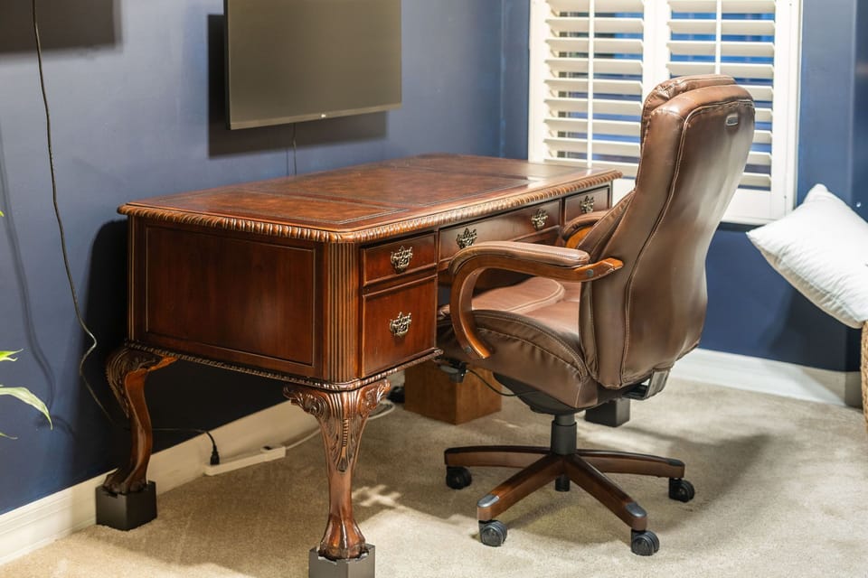 Large executive desk with wall-mounted widescreen monitor and a leather chair. 