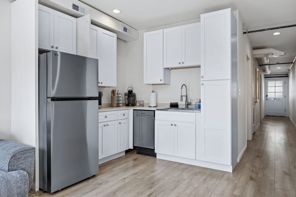 White kitchen with refrigerator, dishwasher, sink, and a view down the hallway.