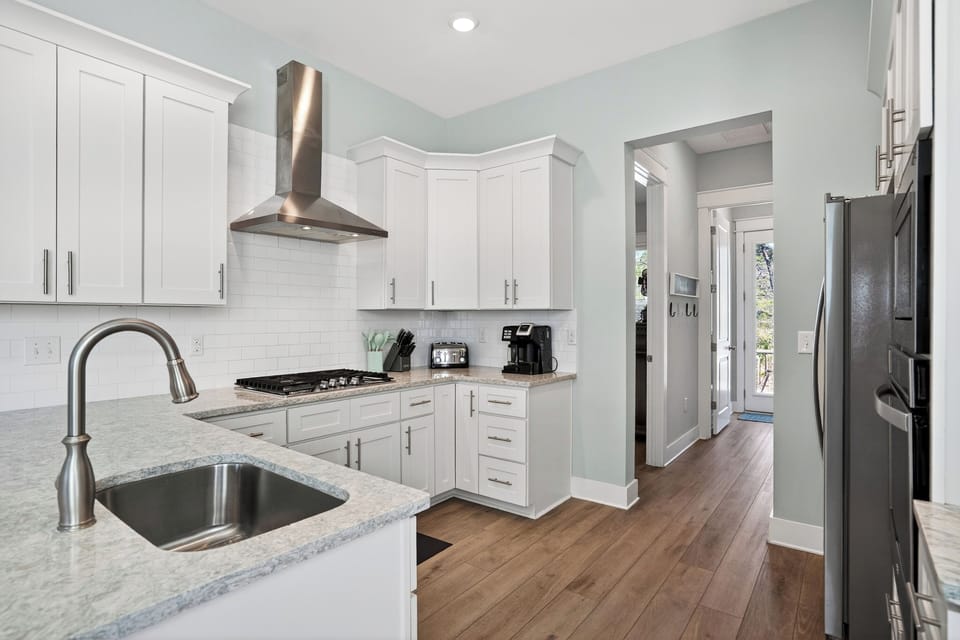 Sleek, sunlit kitchen with crisp white finishes, stainless accents, and a clean flow toward the backyard.