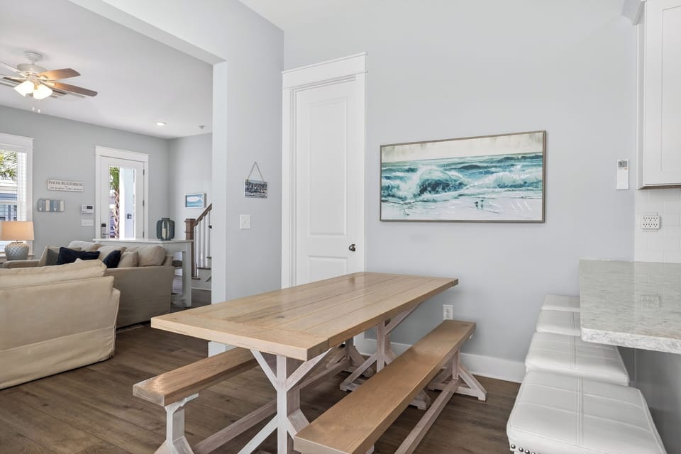 Open‑concept coastal dining area with natural wood tones, soft beachy hues, and sunlight flowing through the home.