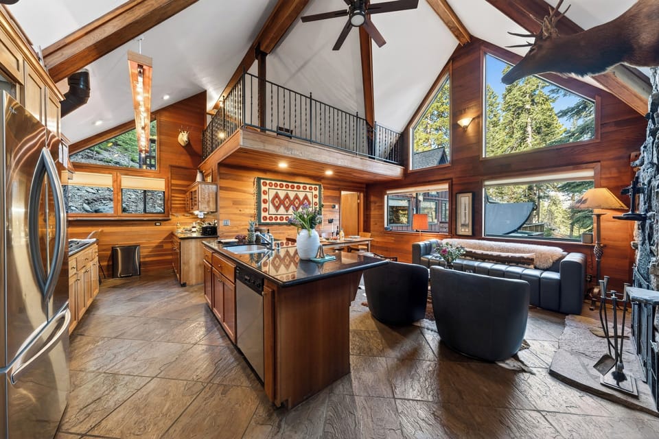 Warm, vaulted cabin interior with towering windows, rustic wood finishes, and a stone fireplace anchoring the open‑concept living space.