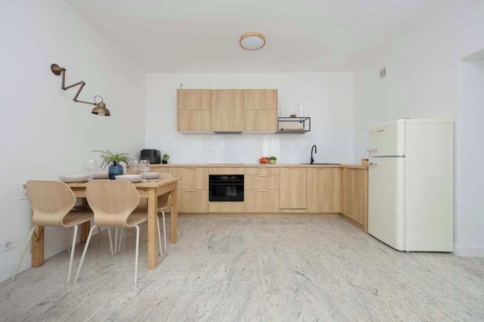 A front view of the kitchenette, highlighting the simplicity and functionality of the natural oak cabinetry. Basic kitchen accessories that facilitate daily life are visible on the countertop.