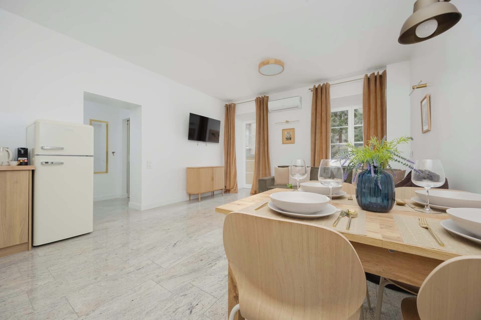 A wide shot of the living area showcasing a white refrigerator and a dining table set for a meal. The light-colored floor reflects light, visually enlarging the entire room.