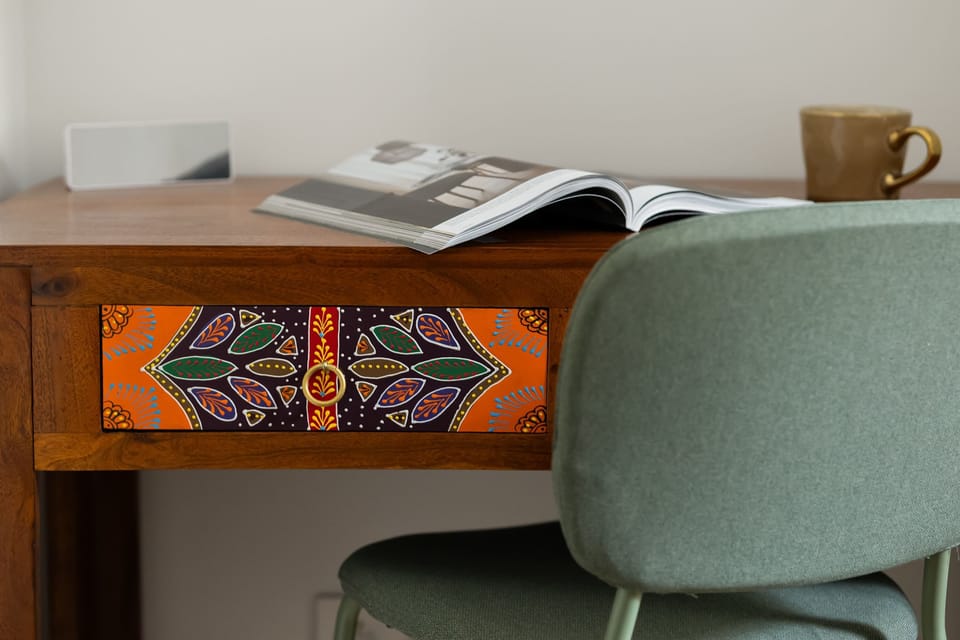 A close-up of a stylish wooden desk with a decorative, painted drawer front and a modern chair. It’s the perfect spot for working on a computer or reading a book.