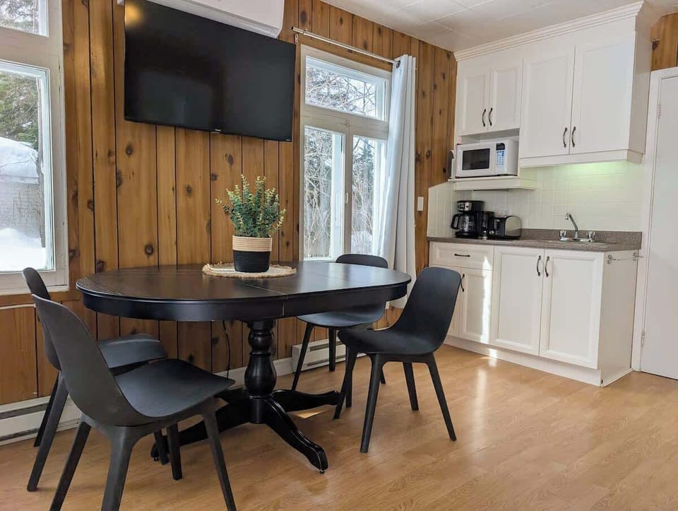 Cet espace comprend un ensemble de salle à manger noir moderne et une cuisinette bien équipée avec des armoires blanches. Que ce soit pour un café matinal ou un souper fait maison, c'est un endroit lumineux et efficace pour tous vos repas.