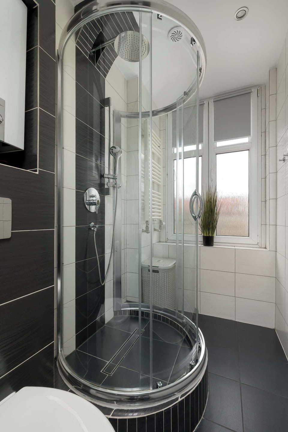 A focused shot of the modern shower cabin with a chrome showerhead and curved glass doors. The black tiles provide a sophisticated and contemporary look.