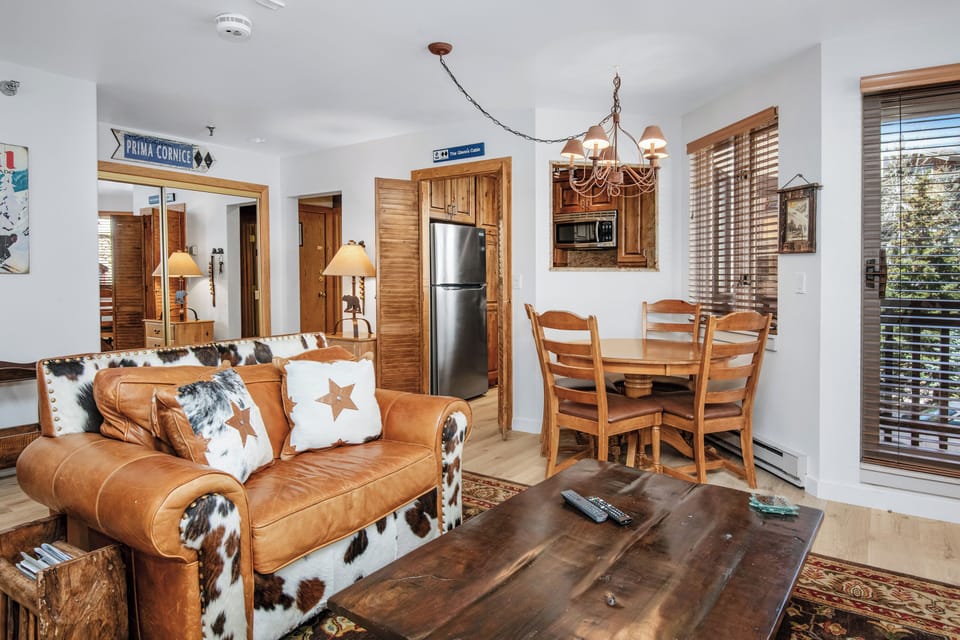Settle into this inviting open-concept space where rustic charm meets mountain comfort. Your cozy leather sofa opens to a dining area and well-equipped kitchen, all bathed in natural light from large windows overlooking the slopes.