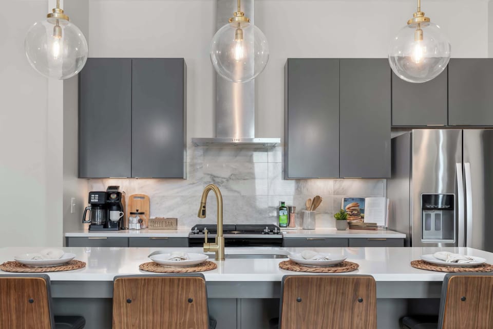 The kitchen island features quartz countertops, brass fixtures, bar seating for four, globe pendant lighting, and a full suite of stainless steel appliances, including a gas range, range hood, and french door refrigerator