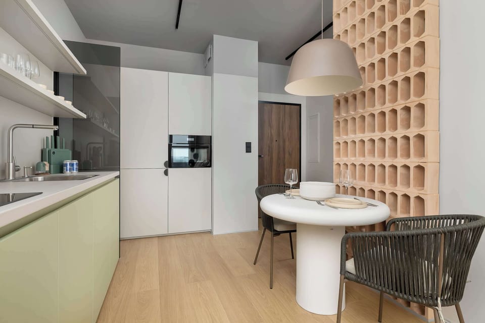 A compact dining area with a round table and modern chairs placed next to a kitchenette. Light wood and soft green tones add warmth and harmony to the space.