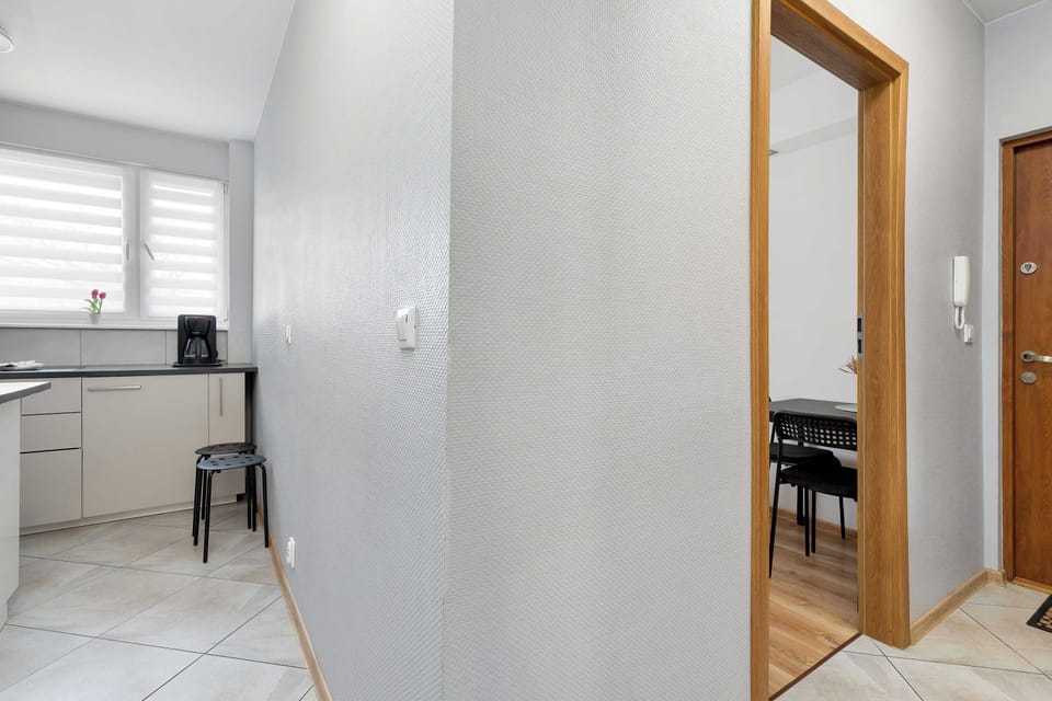 The narrow hallway features light-colored walls and leads toward the kitchen area. A wooden door frame opens into another room with wooden flooring.
