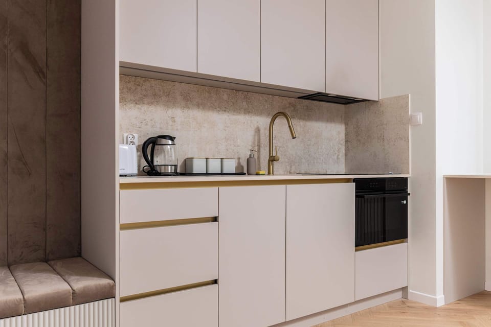 A modern kitchenette with white cabinet fronts and gold hardware, which adds a touch of luxury to the interior. The countertop flows seamlessly into the windowsill, creating additional usable space.