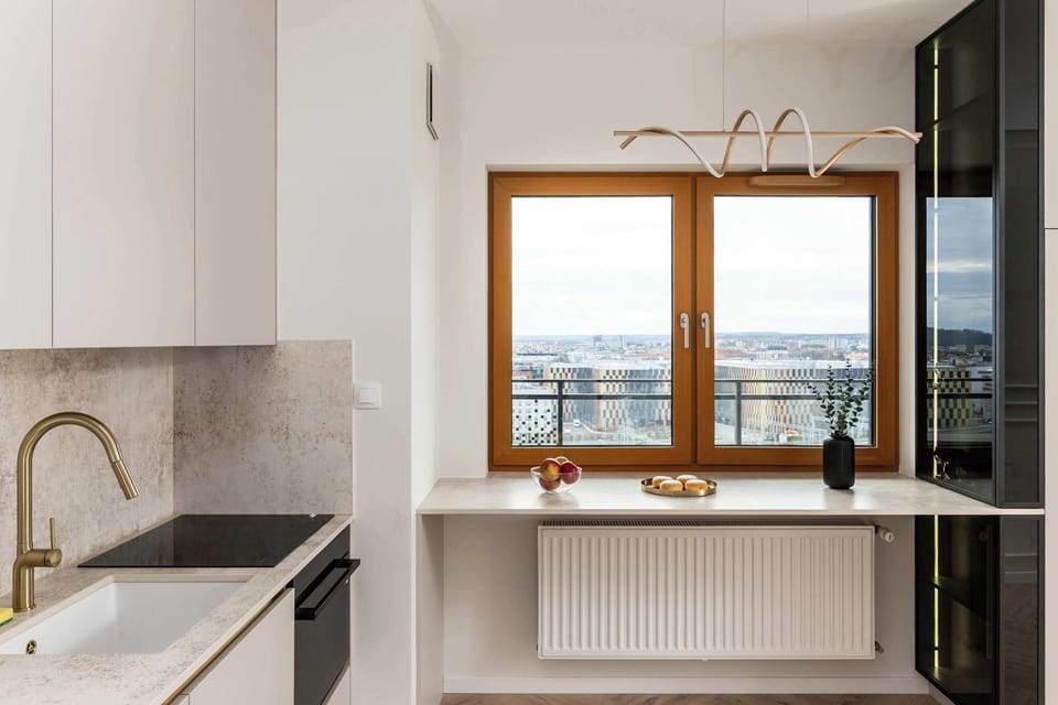 A bright kitchenette with a window overlooking the city skyline, equipped with an induction cooktop and a sink. Under the window is a long countertop, perfect for quick meals.