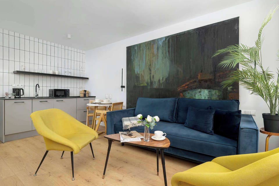 A deep blue sofa is decorated with a patterned throw blanket, sitting beneath an oversized piece of textured wall art. Two yellow armchairs add a bright, sunny contrast to the cooler tones.