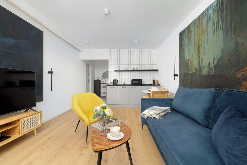 The living room is shown from an angle that includes the media area and the entrance to the kitchen. The yellow armchair and wooden coffee table create a cozy central seating arrangement.