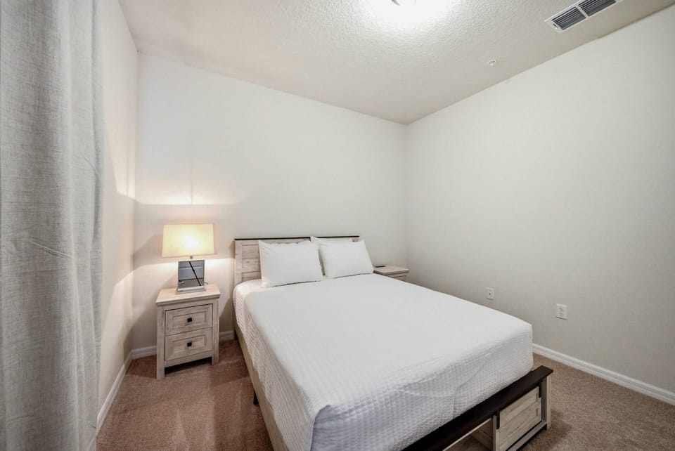 This cozy bedroom features a comfortable bed with crisp white linens, inviting restful nights. A stylish nightstand with a soft lamp adds warmth, while the light-colored walls and plush carpeting enhance the tranquil atmosphere.