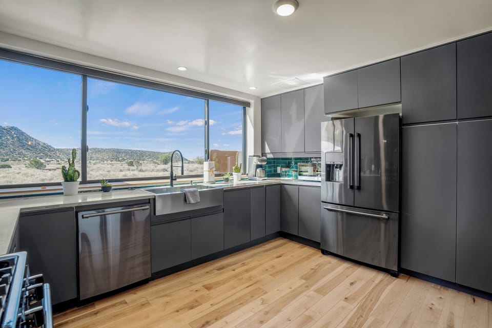 Your modern kitchen features sleek gray cabinets and stainless steel appliances, with stunning desert mountain views through expansive windows.