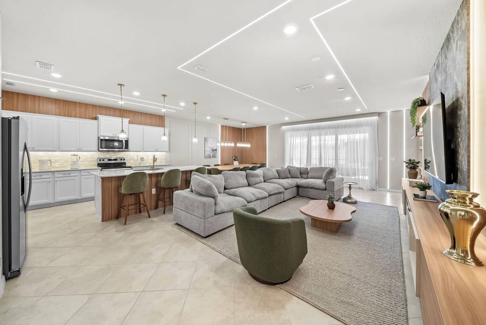 Enjoy a cozy living area with a comfy sectional and stylish green chairs, all warmly lit. The kitchen boasts rich wood cabinetry and modern appliances, perfect for relaxed gatherings with friends and family.
