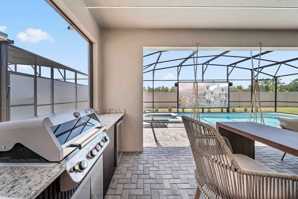 Relax in the sunlit outdoor dining area, featuring a stylish grill and elegant table, perfect for al fresco meals. Enjoy expansive views through the screened enclosure, enhancing your stay by the sparkling pool.