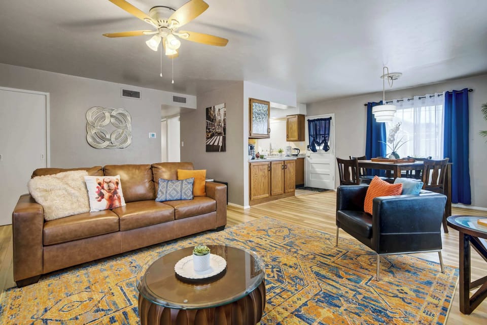 A wider angle reveals the full living room layout, with the sofa, ottoman, and accent chair arranged around the Smart TV for easy gathering. Light wood flooring runs consistently through to the adjacent dining area, tying the main level together.
