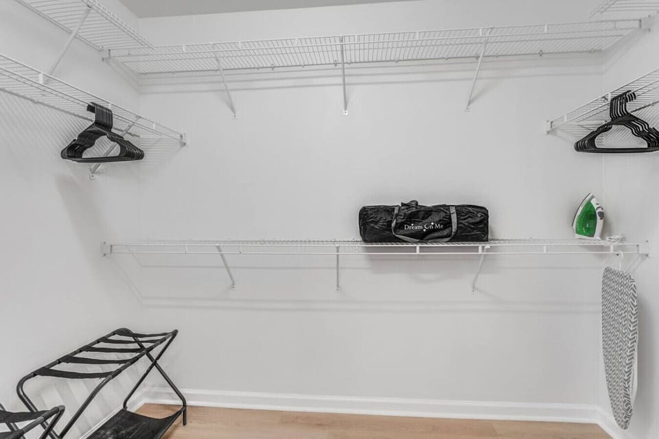 Spacious walk in closet connected to the primary bathroom featuring a pack n play and iron with ironing board.