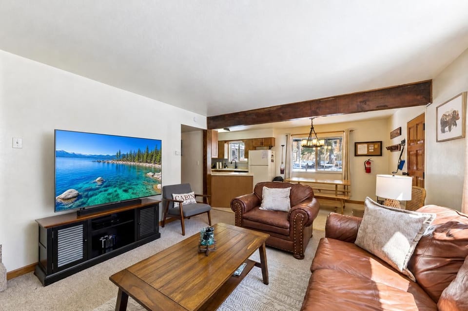 Living area featuring worn leather couch and armchair, wood coffee table, and large flat-screen TV on black console.