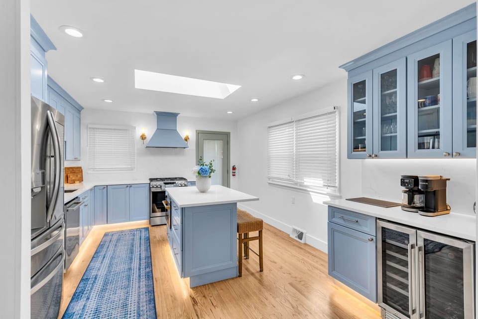 Full chef kitchen with blue shaker cabinets, marble counters, range hood, gas stove, glass-front uppers, beverage fridge, and a dedicated coffee bar.