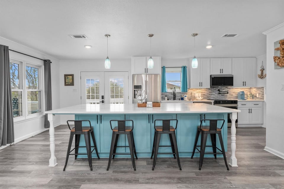 Fully equipped kitchen with large island, bar stools, pendant lighting, and stainless appliances.