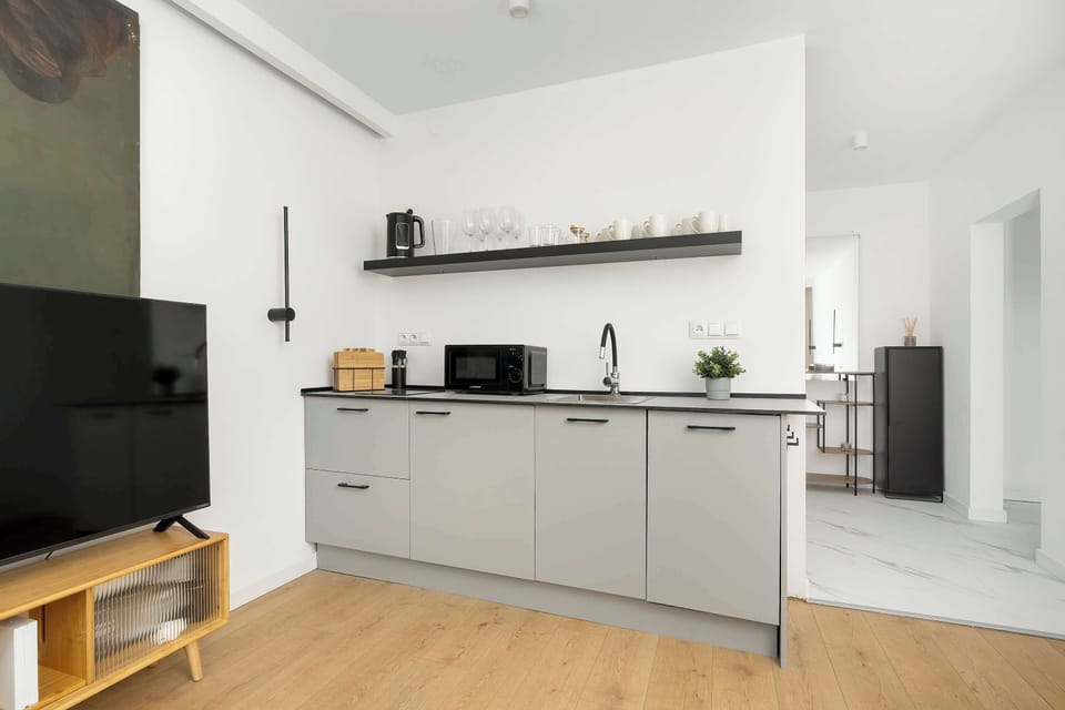 A sleek kitchenette with light-colored cabinets and a wooden countertop. Open shelving displays minimalistic decor, while built-in appliances keep the design streamlined. The space feels functional yet aesthetically pleasing.
