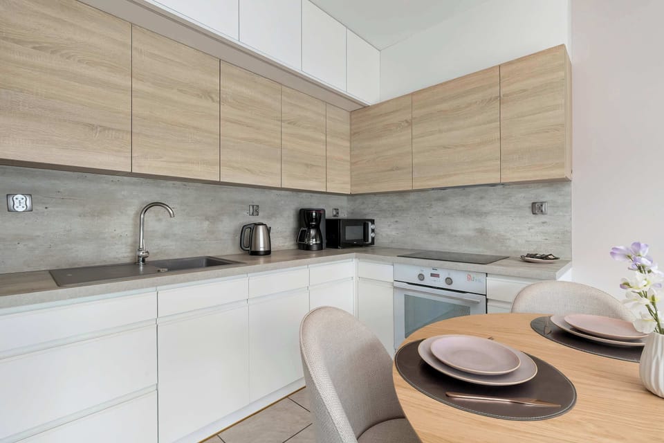 This modern L-shaped kitchen combines sleek white lower cabinets with warm wood-grain upper units. A compact dining area is integrated into the space, featuring a round table set for a meal.