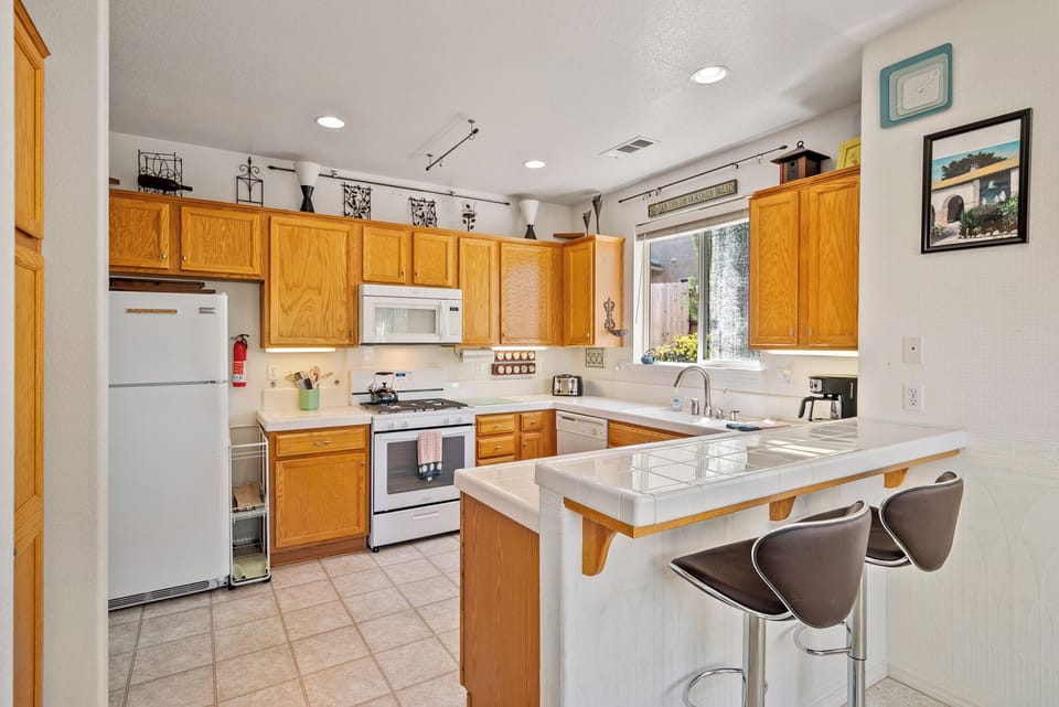 This functional U-shaped kitchen combines classic oak cabinetry with bright white countertops and tiled surfaces. It is fully equipped with modern white appliances, including a Frigidaire refrigerator and a gas range with an overhead microwave.