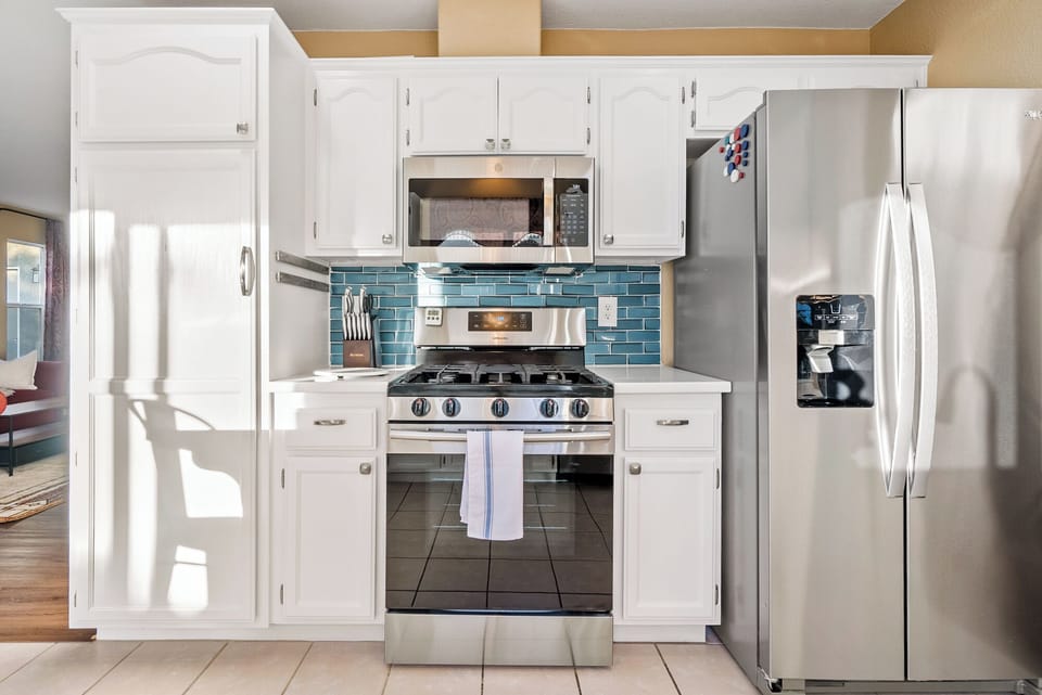 A modern and highly functional kitchen space featuring a large stainless steel French door refrigerator, a matching gas range, and a vibrant blue tile backsplash that provides a stylish contrast to the clean white cabinetry.