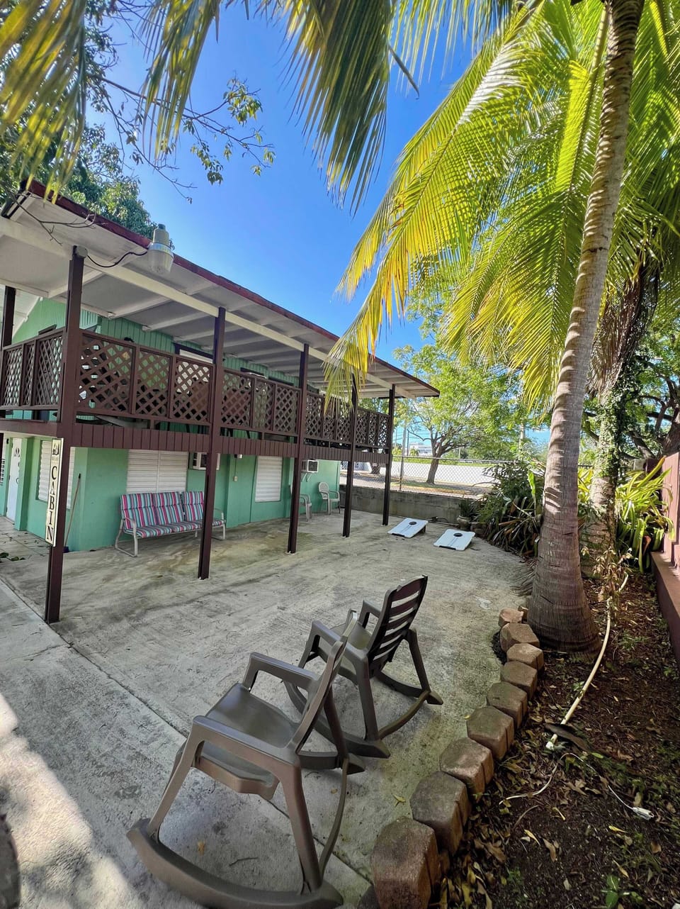 Beachside property with rocking chairs, upper balcony, and palm trees.
