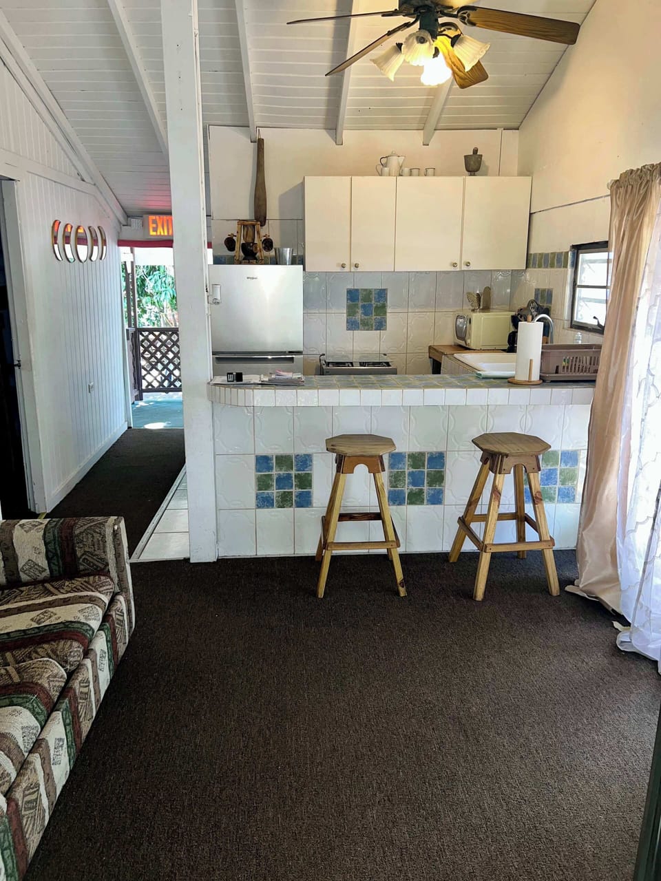 Open living and kitchen area with bar seating, ceiling fan, and natural light.
