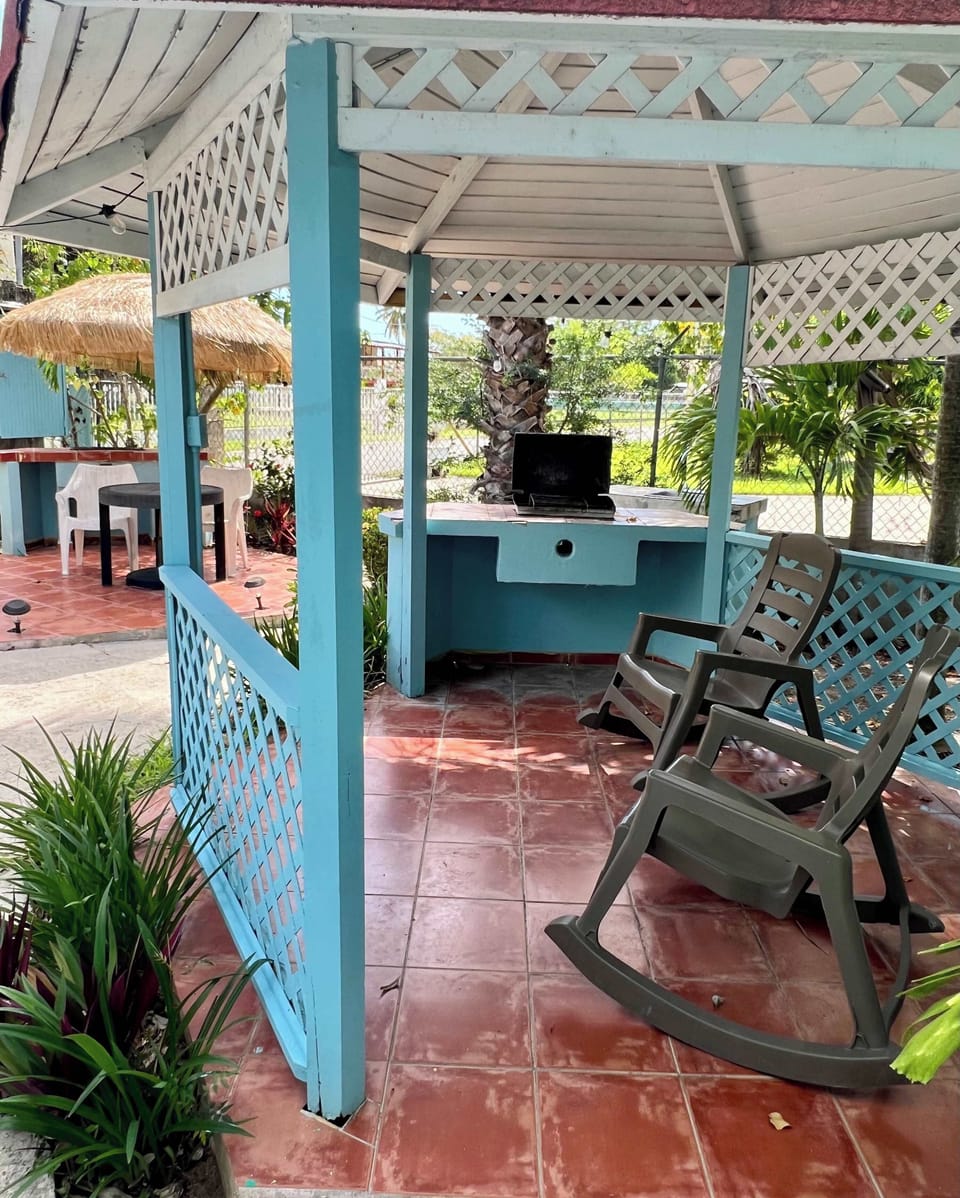 Breezy covered veranda with rocking chair and workspace, surrounded by lush greenery.
