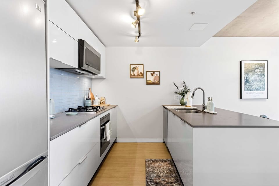 Bright and modern kitchen layout highlighting a gas range, light blue glass subway tile backsplash, minimalist white cabinets, and modern track lighting over light wood floors.