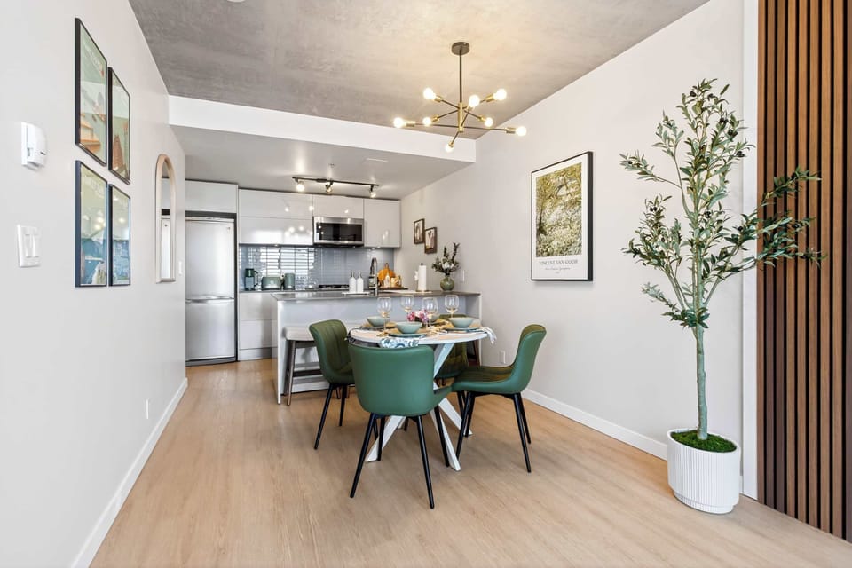 Open-concept apartment interior showcasing a sleek white kitchen and a stylish dining space, beautifully framed by a custom wood slat accent wall and an indoor olive tree.
