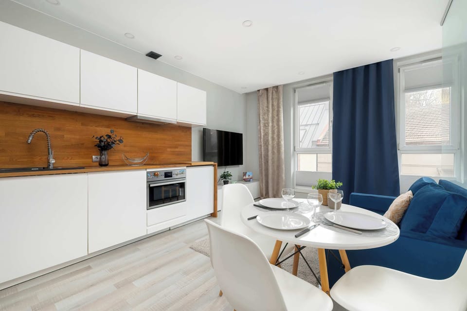 The camera angle emphasizes the dining area and kitchen, highlighting the flow of the open-concept design. Sunlight fills the room from the large windows on the right side.