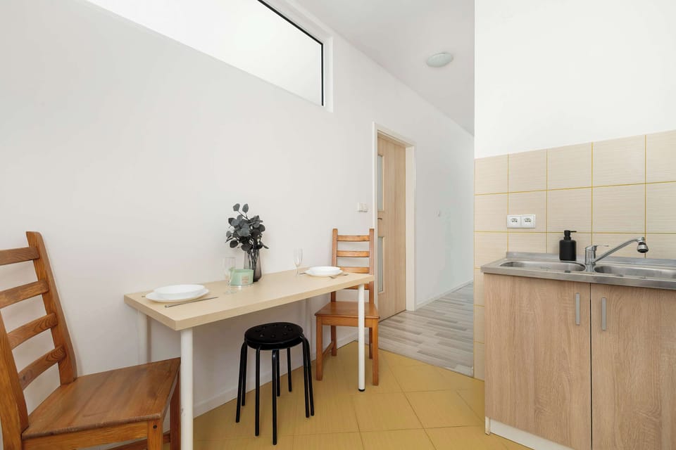 The kitchen's dining nook is shown from another angle, revealing its proximity to the cooking zone. A tall wooden chair and a simple stool provide seating options.