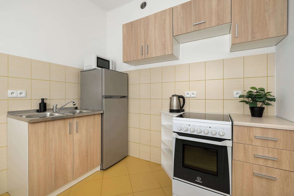 The kitchen is equipped with light wooden cabinets, a silver refrigerator, and a white gas stove. Tiled walls and organized countertops suggest a clean and functional cooking space.