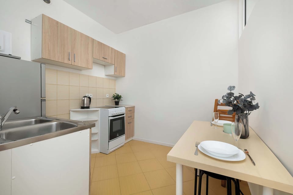 A small dining table with two chairs and a stool is set against a white wall in the kitchen area. The space is efficiently utilized, offering a spot for quick meals or breakfast.