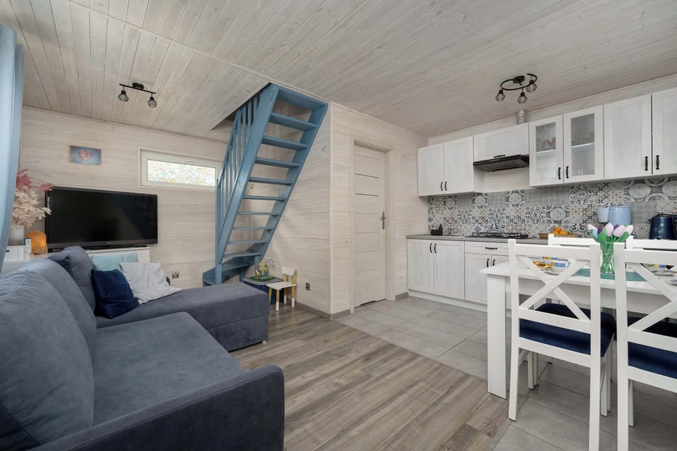A bright living area with a cozy sofa placed near a small dining table and chairs. The space connects seamlessly with a compact kitchenette.