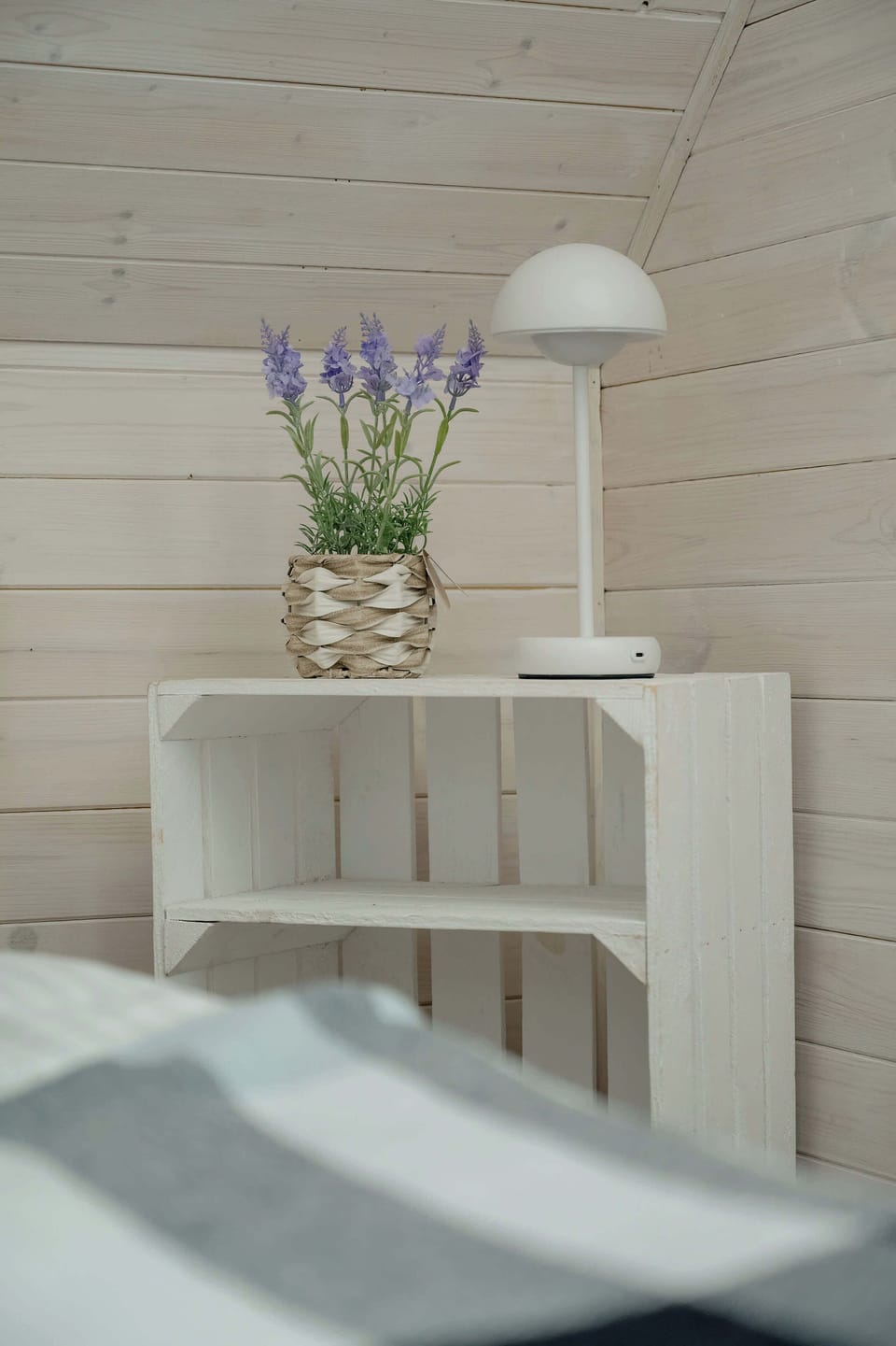 A bedside table with a lamp and a small vase of flowers, creating a warm and relaxing ambiance. The soft lighting and natural elements enhance the cozy feel of the room.