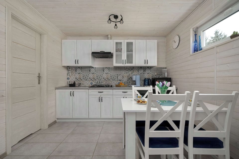 A dining area with a white table set for a meal, surrounded by matching chairs. The kitchenette behind it is neatly arranged with modern cabinets and essential appliances.