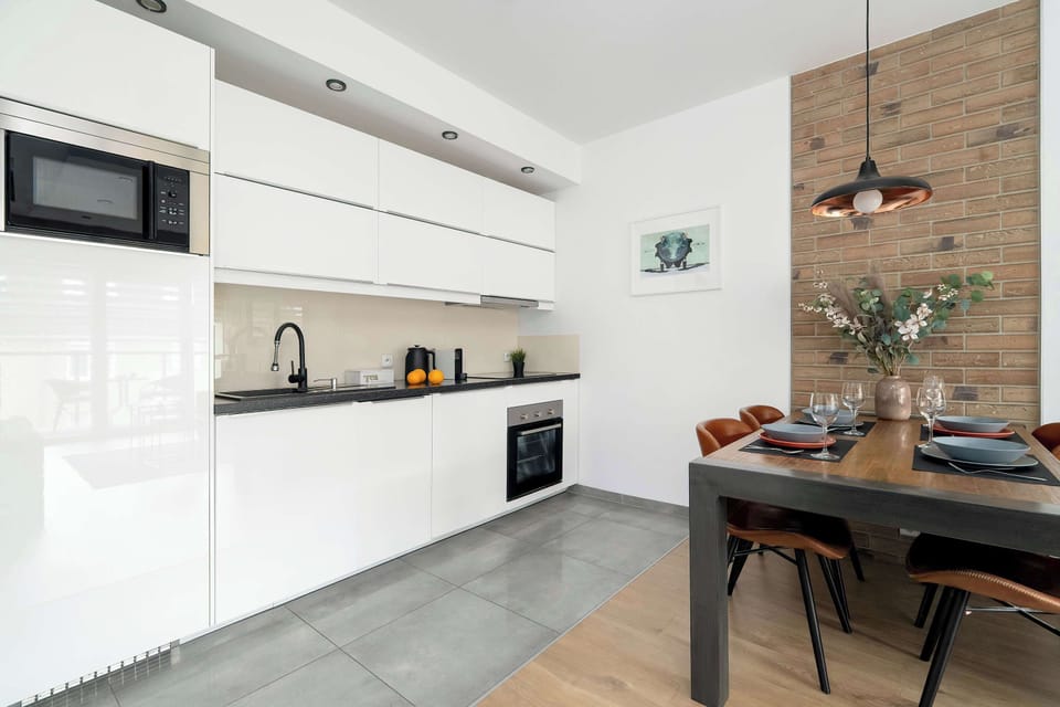 A bright kitchen corner shows the clean lines of white cabinetry and a dark backsplash. The overhead lighting is integrated into the ceiling to provide a clean, modern look.