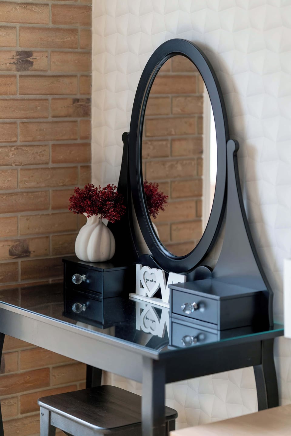 A stylish vanity area features a tall oval mirror mounted on a dark, textured wall. The black table below holds decorative items, creating a dedicated space for grooming.