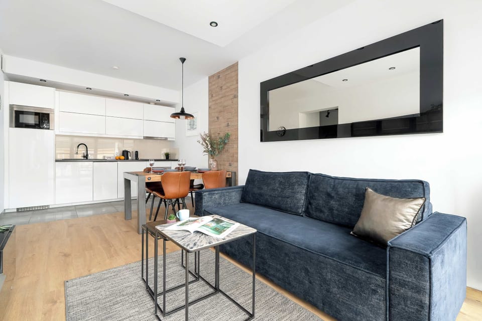 An open-concept living space connects the kitchen and dining area, featuring a large horizontal mirror that reflects the room's depth. The blue sofa serves as a bold focal point against the light-colored walls.