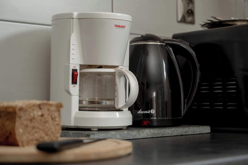 A kitchen counter with a coffee machine, kettle, and cups. Practical setup for making drinks.