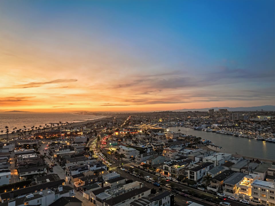 Experience the magic of a Newport Beach sunset from above. This breathtaking aerial shot captures the city lights beginning to glow against the backdrop of the Pacific Ocean and the serene harbor.
